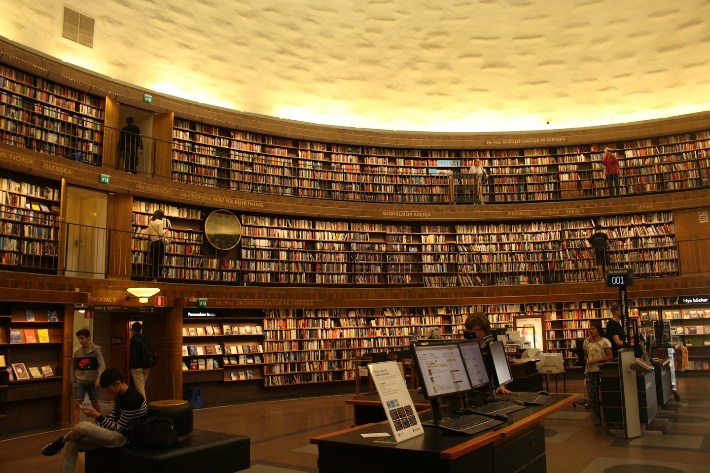 Persone sfogliano libri e usano computer all'interno di una biblioteca circolare.